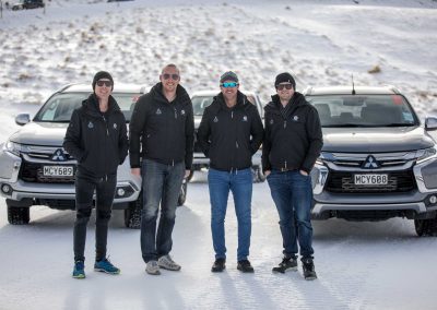 group of guys on snow in front of cars