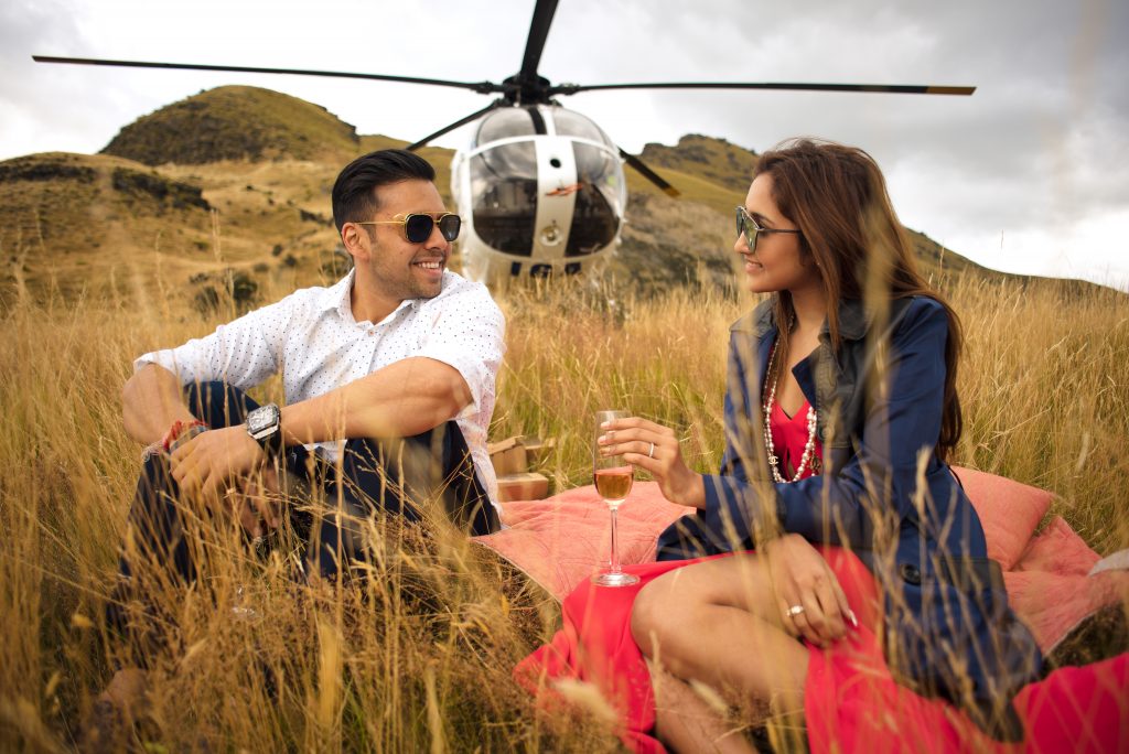 Couple sitting in grass by helicopter Queenstown portrait photography
